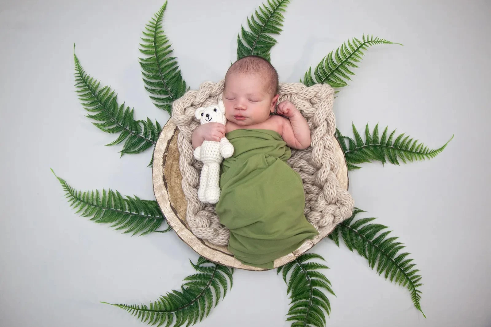 Newborn baby holding stuffed bear surrounded by green leaves, captured by Nicole Marie Photography in Port St. Lucie, Florida