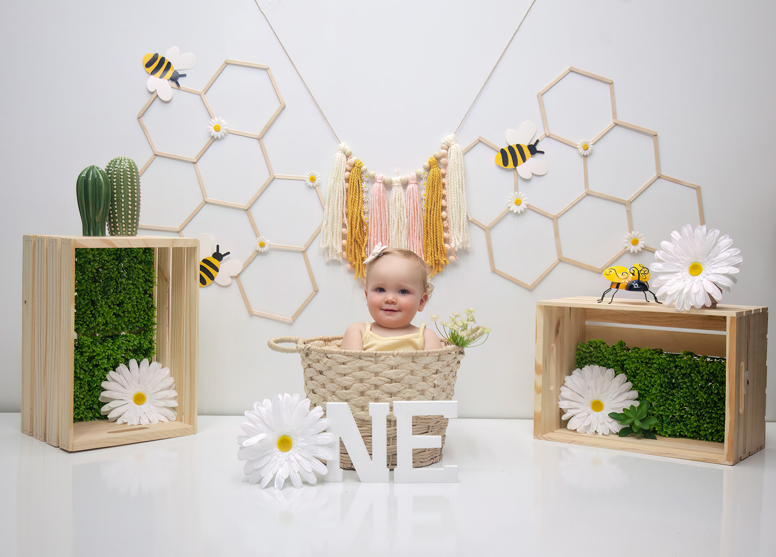 Smiling baby sitting in basket in a bees and flowers setting