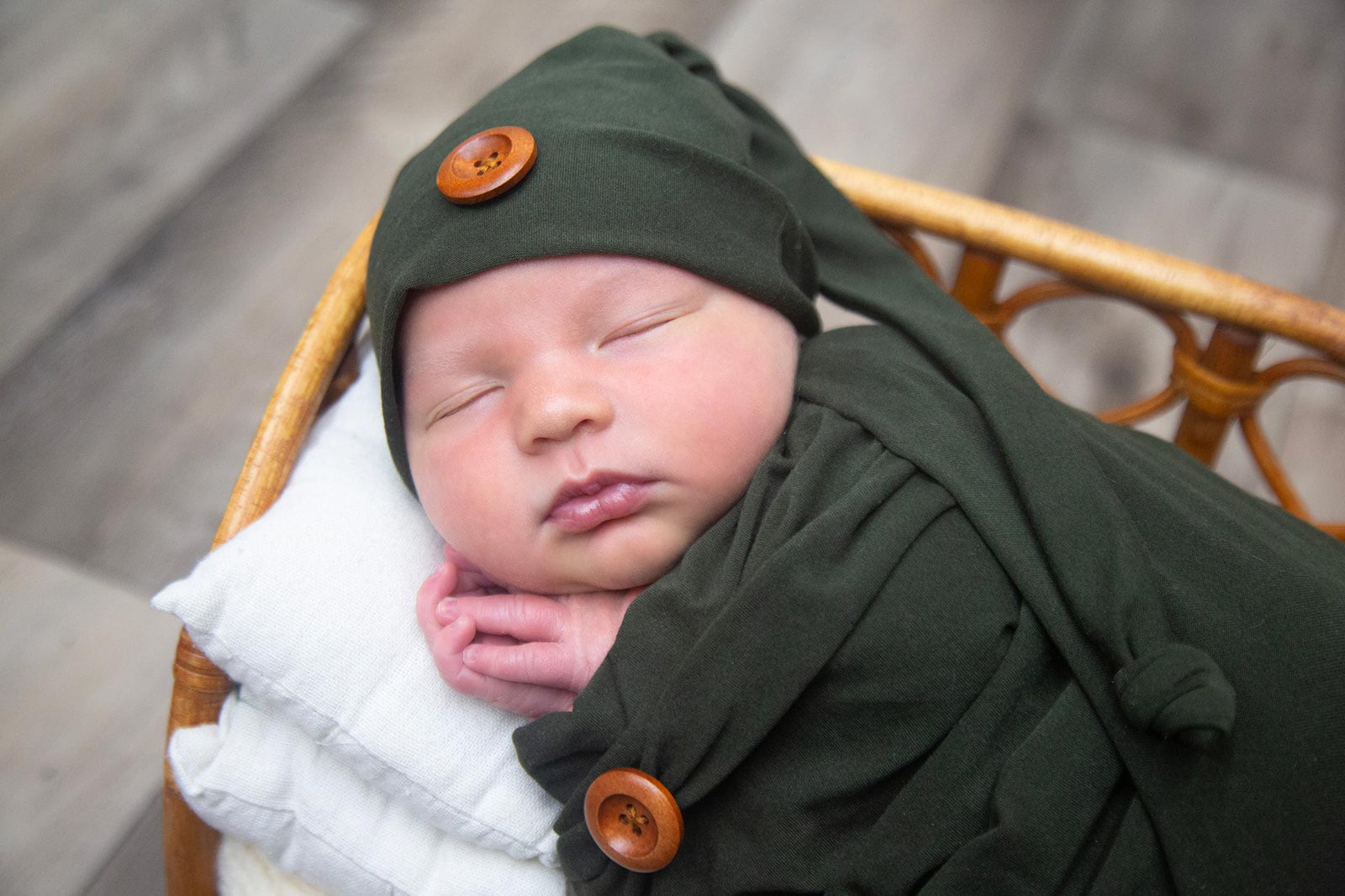 Sleeping newborn baby wrapped in a green blanket, laying on a pillow in a basket
