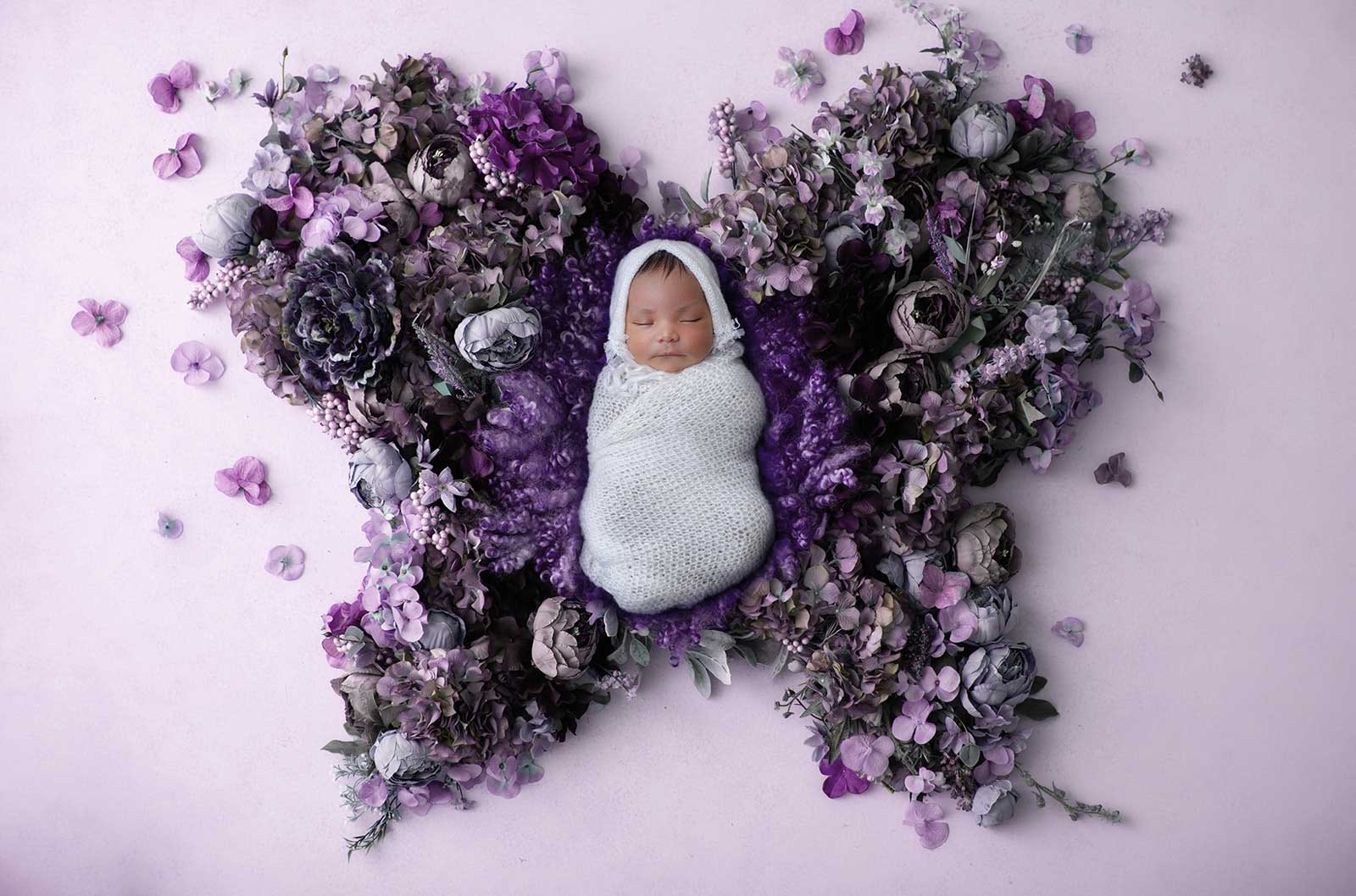 Newborn baby wrapped in a white blanket placed on a decoration of flowers shaped as wings of a butterfly