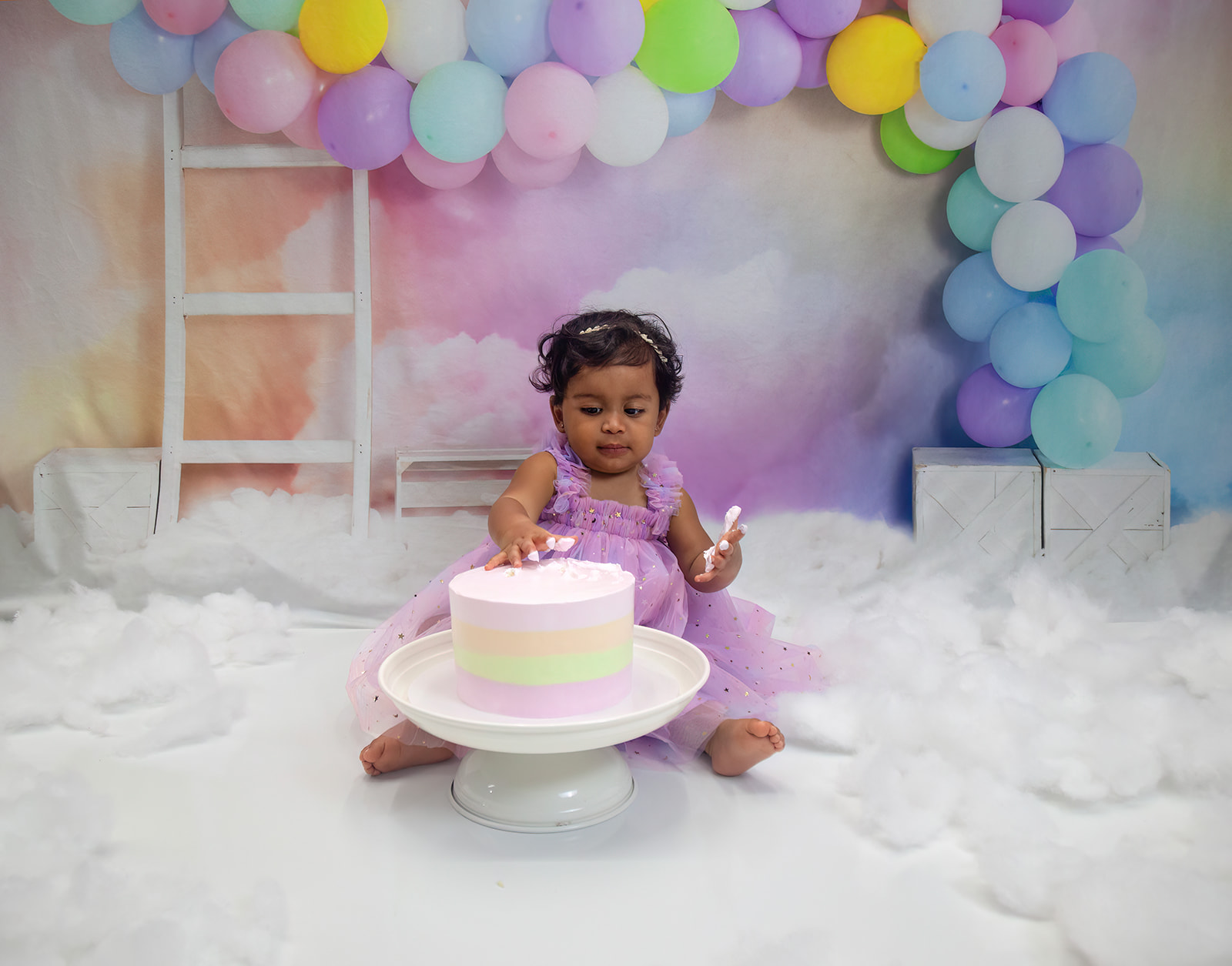 Baby sitting behind cake with hands in it with cloud decorated setting