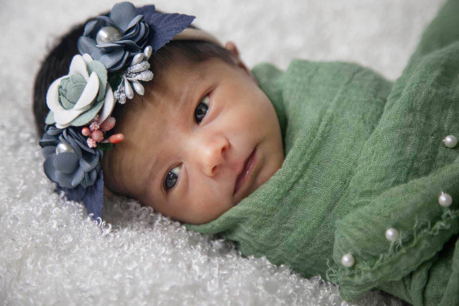 Newborn baby in green wrapping gazing off to the side
