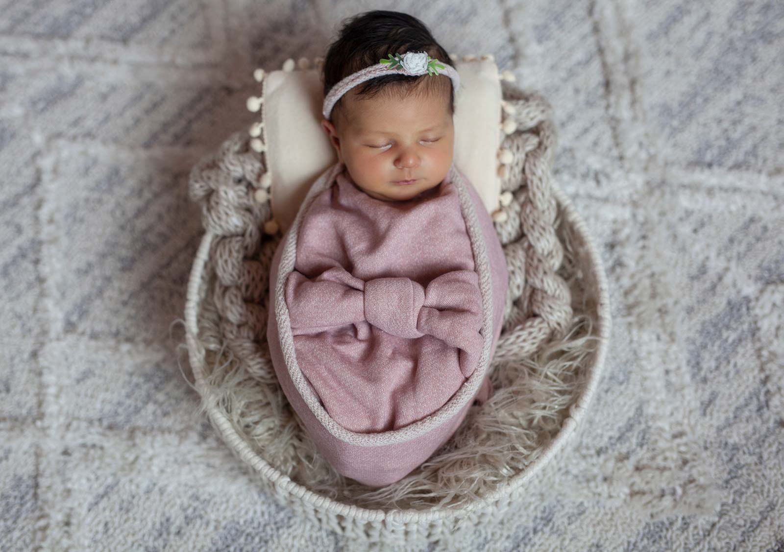 Newborn baby wrapped in pink blanket while laying in basket sleeping