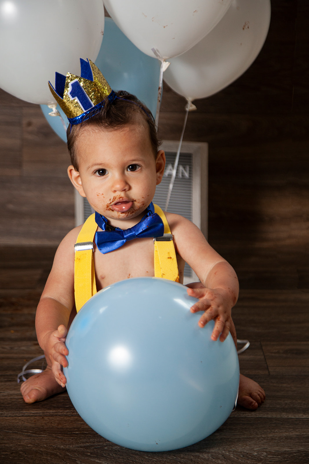 Baby with cake on face is holding a balloon while staring at the camera