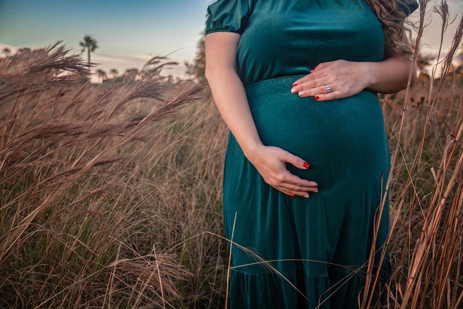 Pregnant woman holding her belly while standing a field of long grass