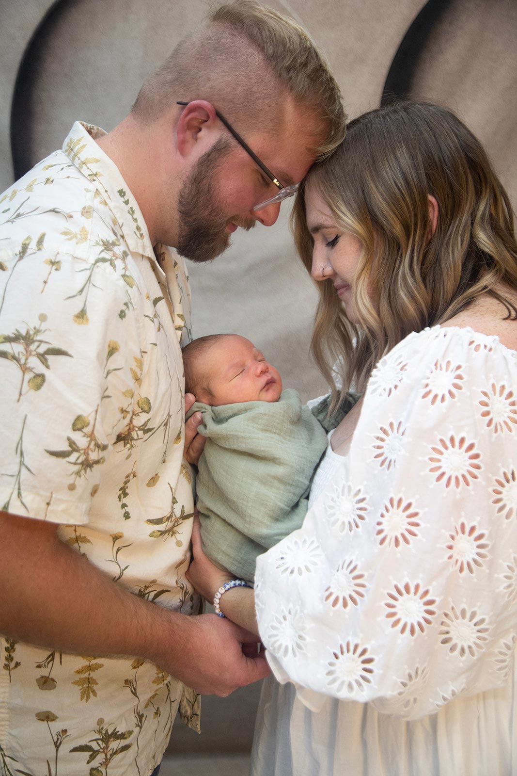 Married couple gently touching heads while holding their newborn baby
