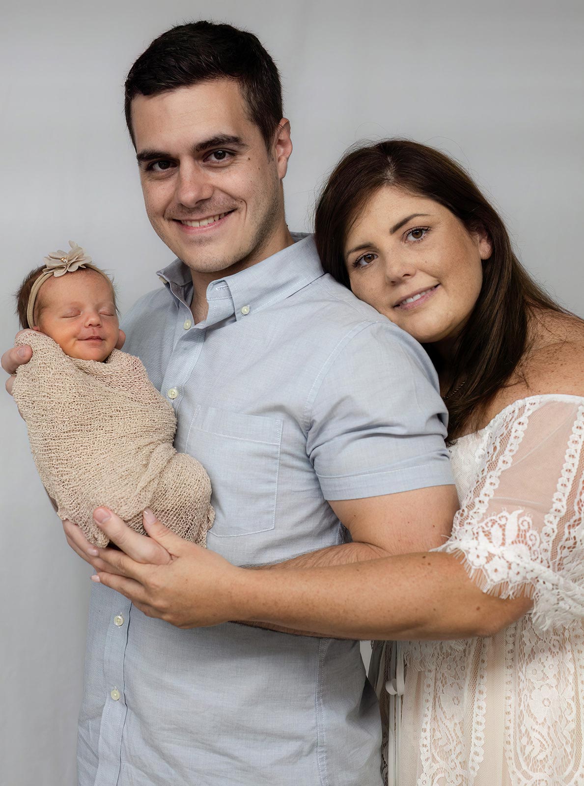 A father and a mother hugging and smiling while holding their newborn baby
