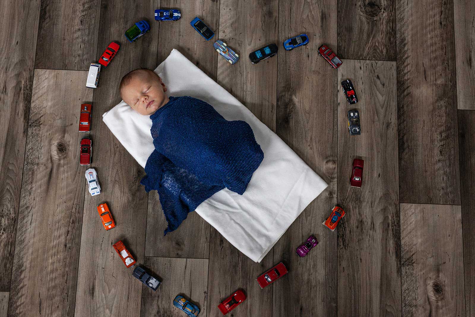 Newborn baby wrapped in blue surrounded by cars placed in heart shape