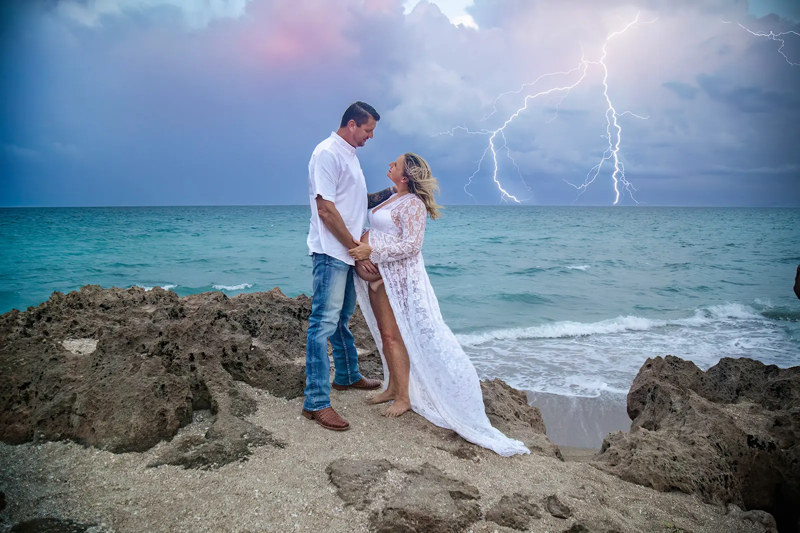 Man and pregnant woman standing on beach with lightning striking in the background, captured by Nicole Marie Photography in Port St. Lucie