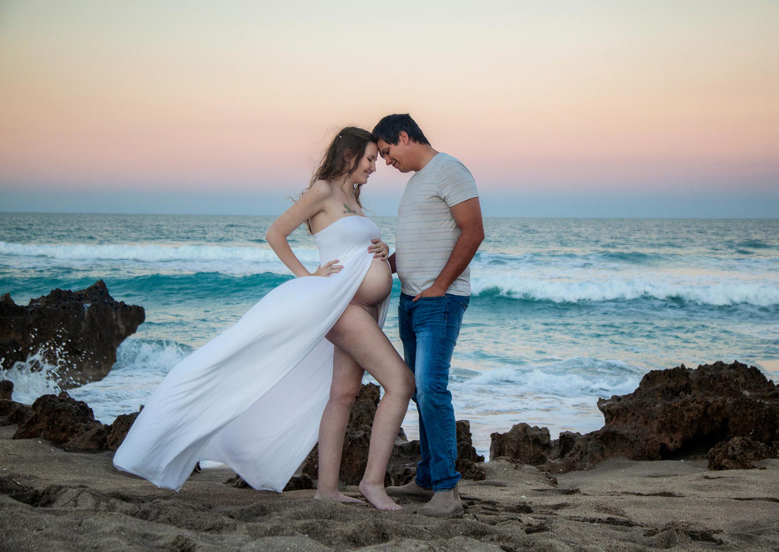 Man and pregnant wife gently leanign on each other while on the beach