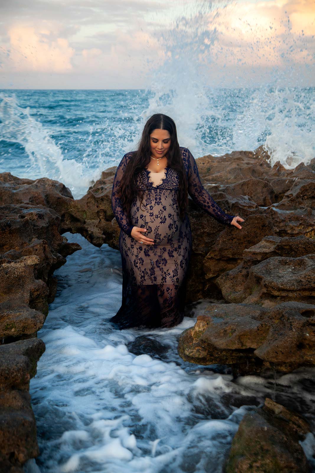 Pregnant woman in black dress standing in stream by the ocean