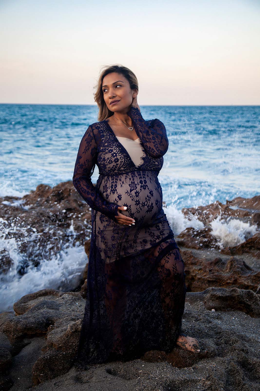 Pregnant woman in black dress standing on beach with waves crashing