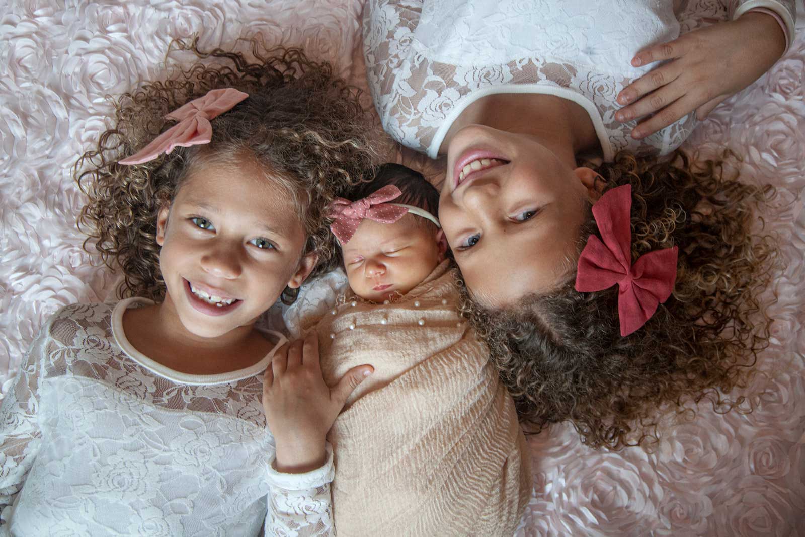 Two children laying down and smiling at the camera with baby between them